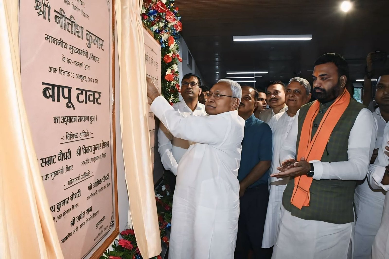 Bihar's Chief Minister Nitish Kumar inaugurating the 'Bapu Tower' in Patna, placing flowers at Mahatma Gandhi’s statue with the towering structure in the background. The modern tower, surrounded by greenery, stands tall with dignitaries and spectators celebrating the event. A tree-planting ceremony also takes place near the tower, emphasizing environmental sustainability.